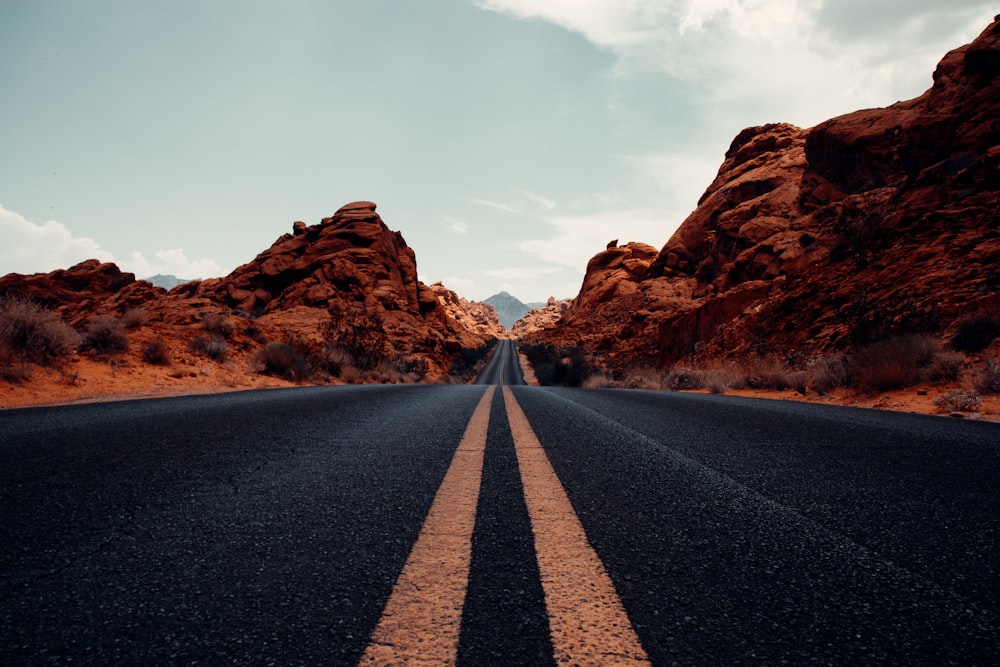 black asphalt road between brown rock formation under white clouds during daytime