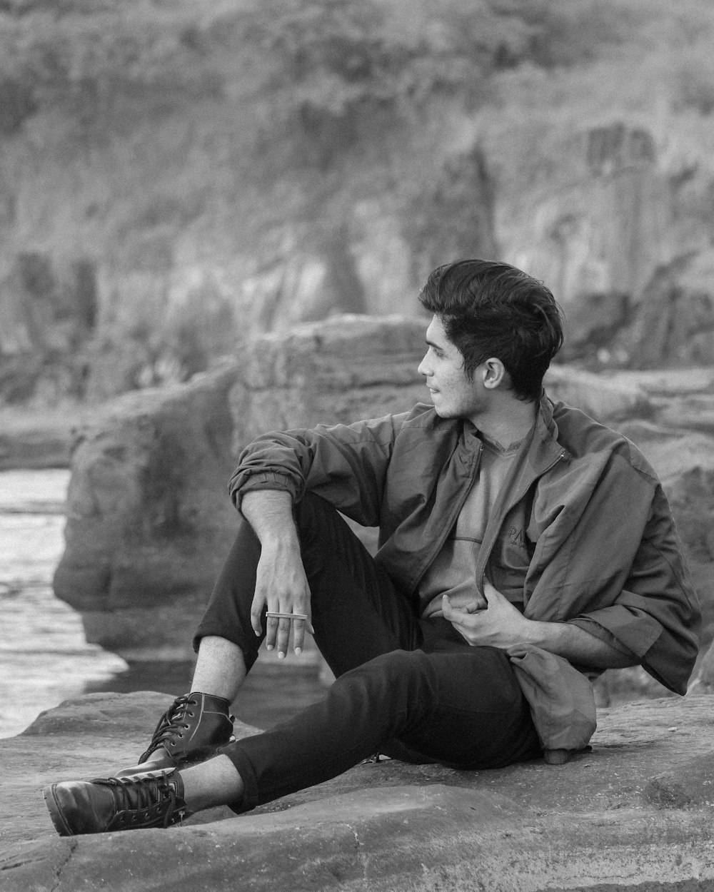 a black and white photo of a man sitting on a rock