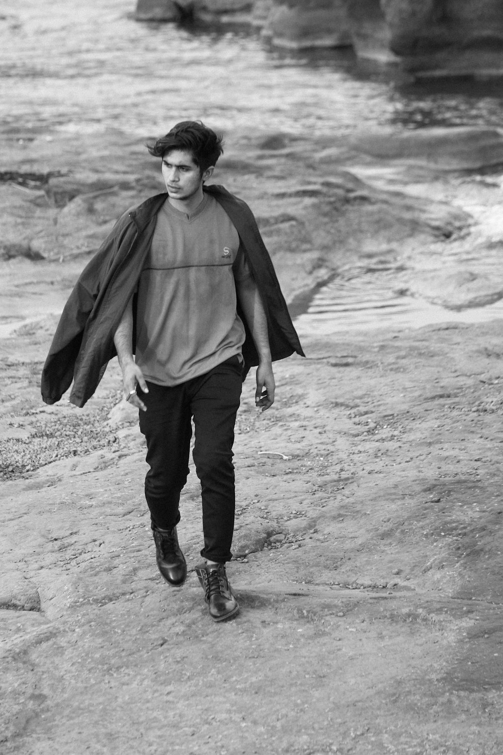 a black and white photo of a man walking on a beach