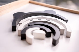 A set of nested, semi-circular, wooden blocks in shades of black, white, and gray, arranged to resemble a panda face. The minimalist design highlights the panda's eyes and ears, creating a playful, abstract representation.