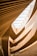 An architectural interior featuring multiple layers of wooden slats and curved structures, which create a flowing, organic pattern. Natural light filters through a large skylight above, highlighting the warm hues of the wood and the gentle curves of the design.