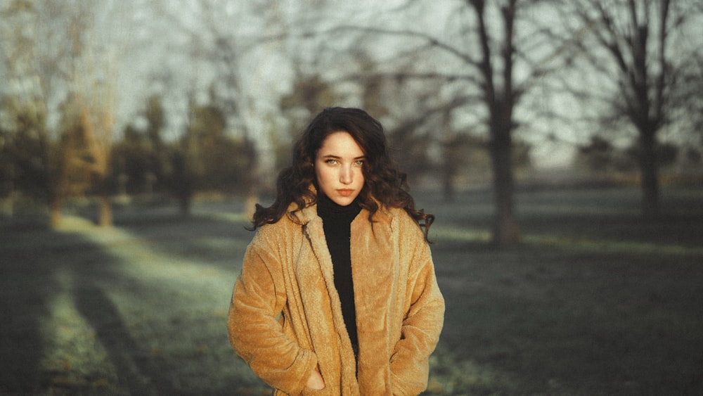 woman in brown coat standing near bare trees during daytime