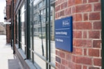 A brick building with a blue sign indicating the location of the Department of Sociology at the University of Oxford. The sign points toward the main entrance, which is in the direction of the glass windows reflecting the opposite street.