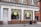 A storefront labeled 'Cantay House' that houses 'Oxford Audio Consultants' with large arched windows. The shop appears to be in an older brick building with white paint surrounding the windows and door. A woman in a green dress is walking on the sidewalk, and a public trash can is visible nearby.