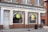 A storefront labeled 'Cantay House' that houses 'Oxford Audio Consultants' with large arched windows. The shop appears to be in an older brick building with white paint surrounding the windows and door. A woman in a green dress is walking on the sidewalk, and a public trash can is visible nearby.
