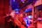 A large industrial facility filled with machinery and metal structures. The space is illuminated by a combination of red and blue lighting, creating a vibrant and futuristic atmosphere. The ceiling is high and expansive, supported by metal beams. Various industrial components and equipment are visible throughout the space, contributing to a complex and busy scene.