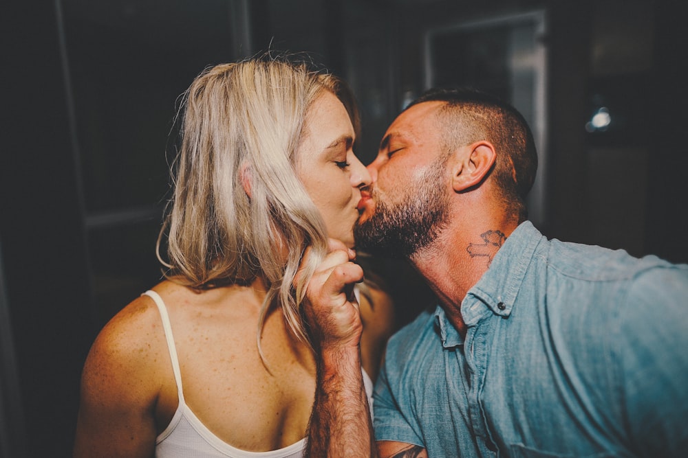 hombre en camisa azul abotonada besando a mujer en top blanco de tirantes finos