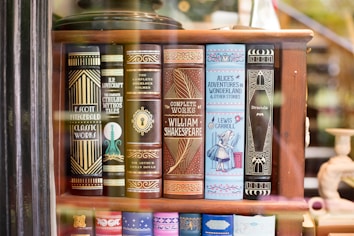 A bookshelf showcasing a collection of classic literature with ornate book covers. Featured titles include works by Fitzgerald, Lovecraft, Doyle, Shakespeare, Carroll, and Stoker. The covers are elaborately designed, with some featuring illustrations like a keyhole and an image of Alice from Alice's Adventures in Wonderland.