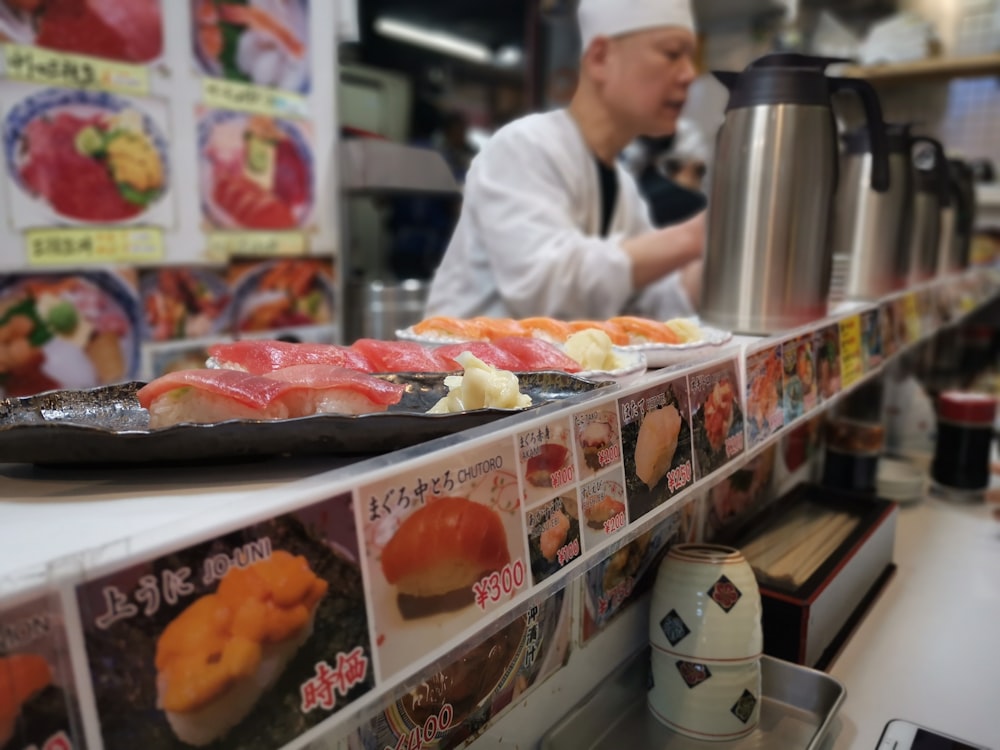 uomo in uniforme bianca da chef in piedi davanti al bancone dell'esposizione di alimenti