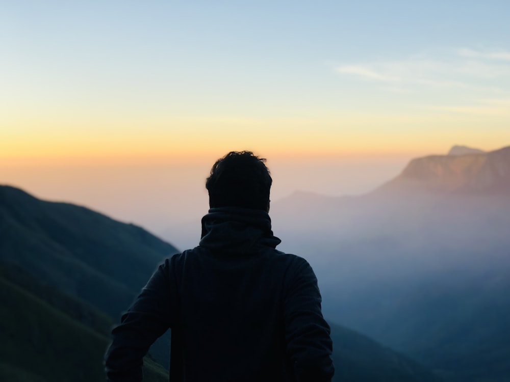 man in black hoodie standing on top of mountain during sunset