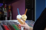 Colorful ice cream scoops in a waffle cone held by a smiling customer.