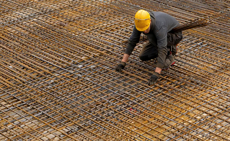 Worker tying rebar across a wide foundation grid before the pour