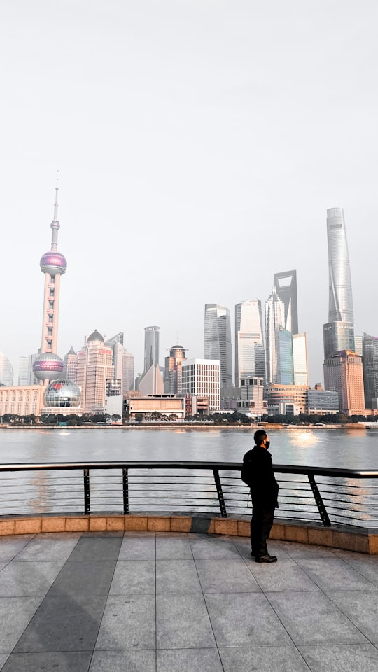 man in black jacket sitting on bench near body of water during daytime in The Bund China