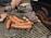 A barbecue grill is loaded with an assortment of meats, including sausages, ribs with charred edges, and a larger piece of meat that appears to have seasoning or a crust. The meats are positioned on the grates, demonstrating a well-cooked, smoky appearance.
