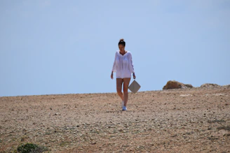 woman in white dress walking on brown sand during daytime