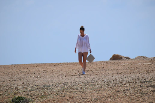 woman in white dress walking on brown sand during daytime