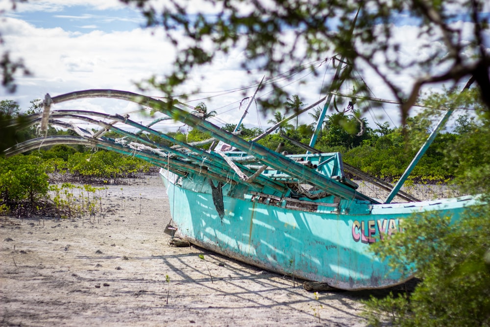teal and white boat on beach shore during daytime