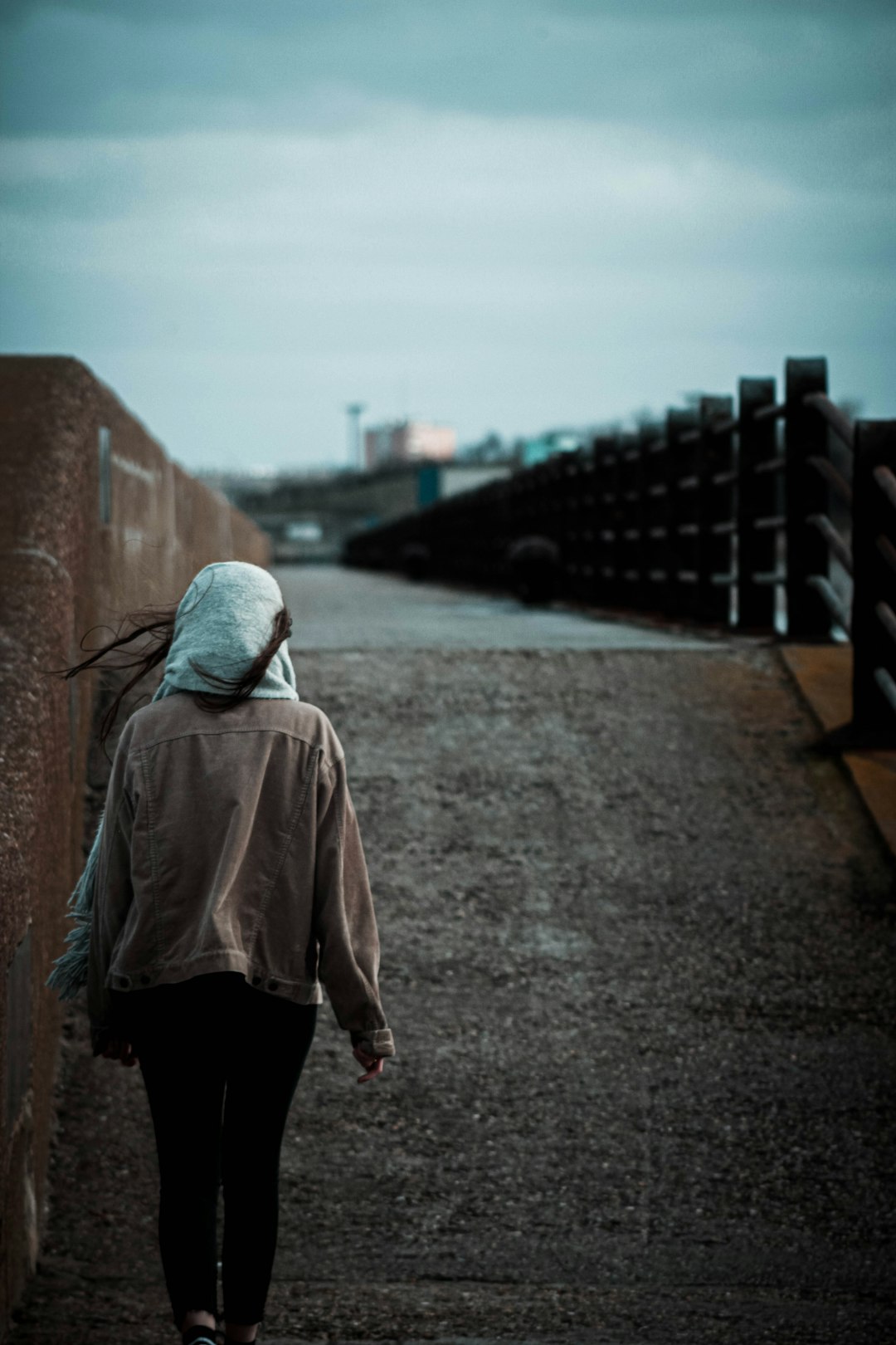 person in brown hoodie standing on bridge during daytime