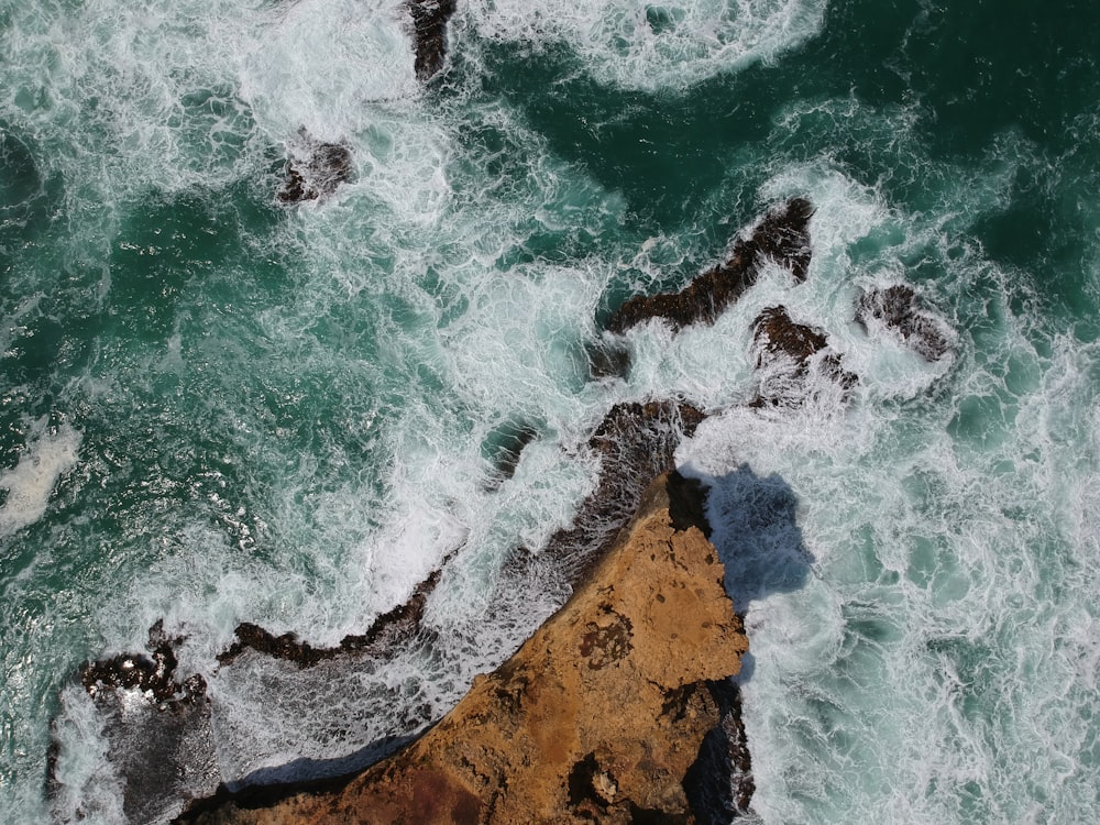 aerial view of ocean waves crashing on brown rocky shore during daytime