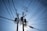 A network of electrical power lines spreading out from utility poles against a clear blue sky. The poles are equipped with transformers and other electrical hardware, creating an intricate pattern of wires overhead.