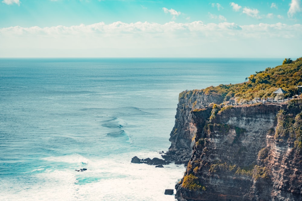 Formation rocheuse brune et verte au bord de la mer bleue sous un ciel nuageux bleu et blanc pendant la journée