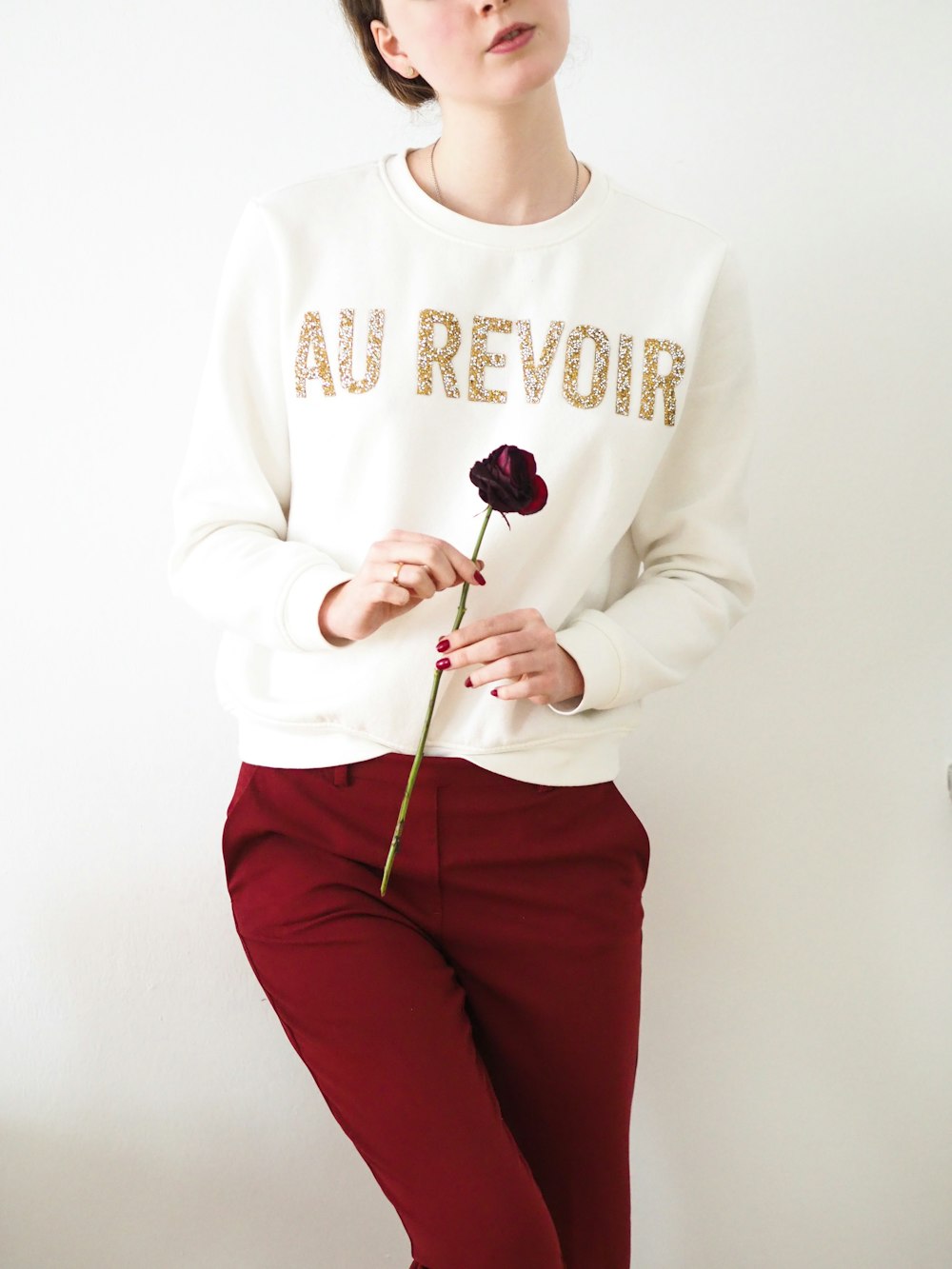 woman in white sweater and red pants holding black and white lollipop