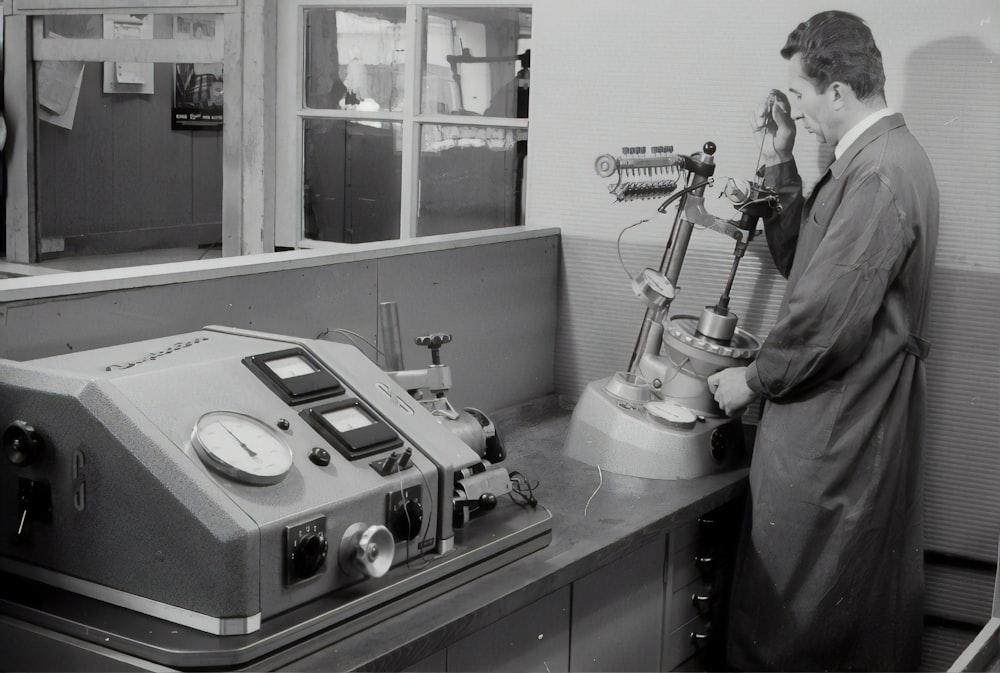 grayscale photo of man standing in front of sewing machine