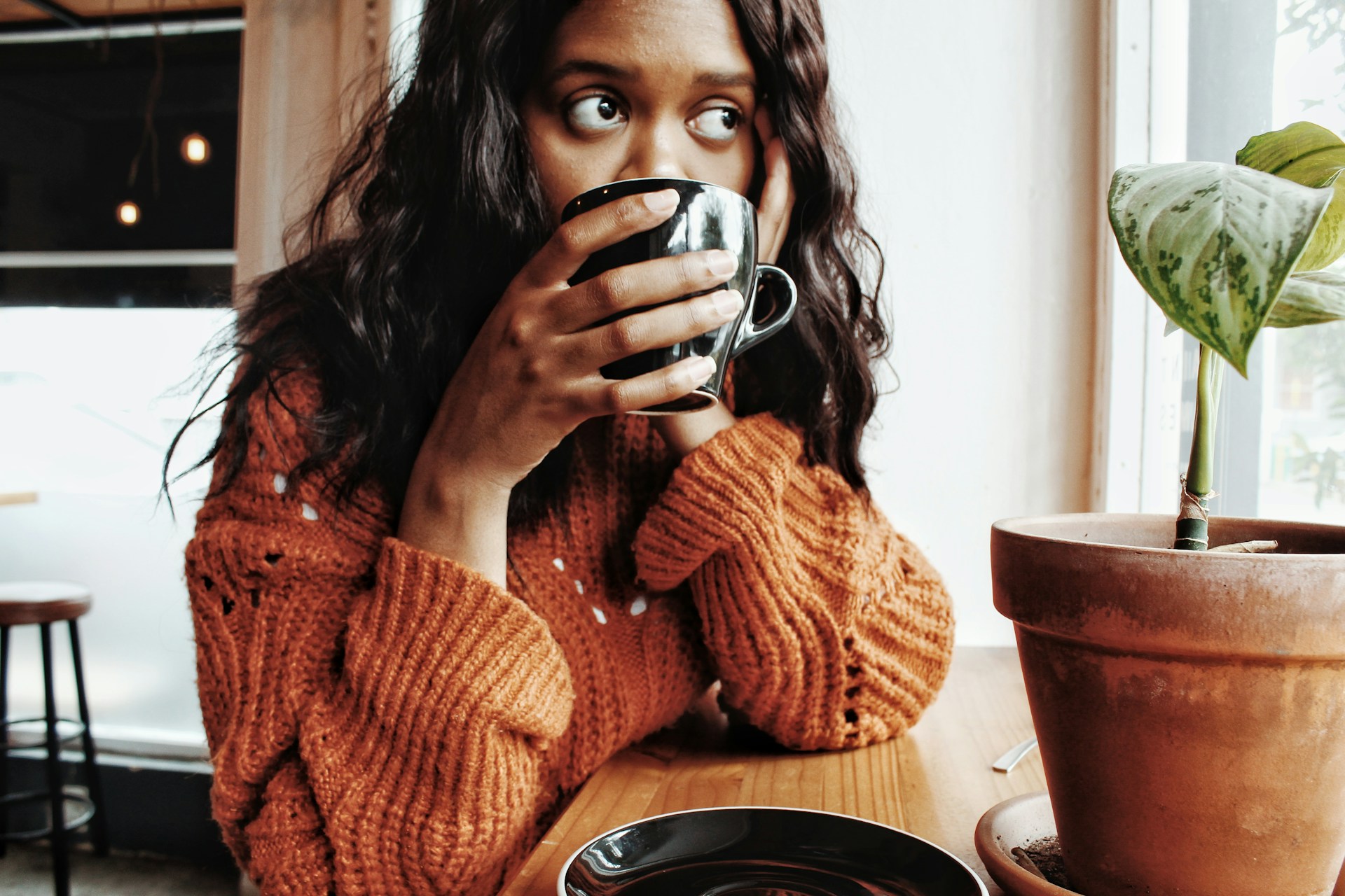 woman in orange knit sweater holding black ceramic mug