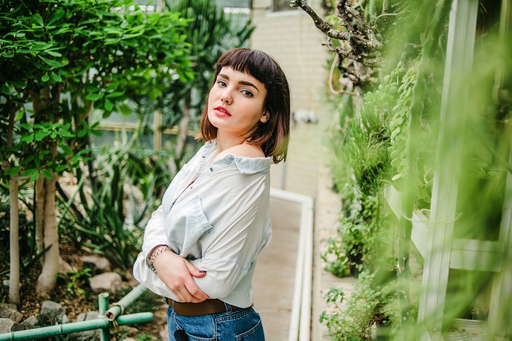 woman in white dress shirt and blue denim jeans standing near green plants during daytime