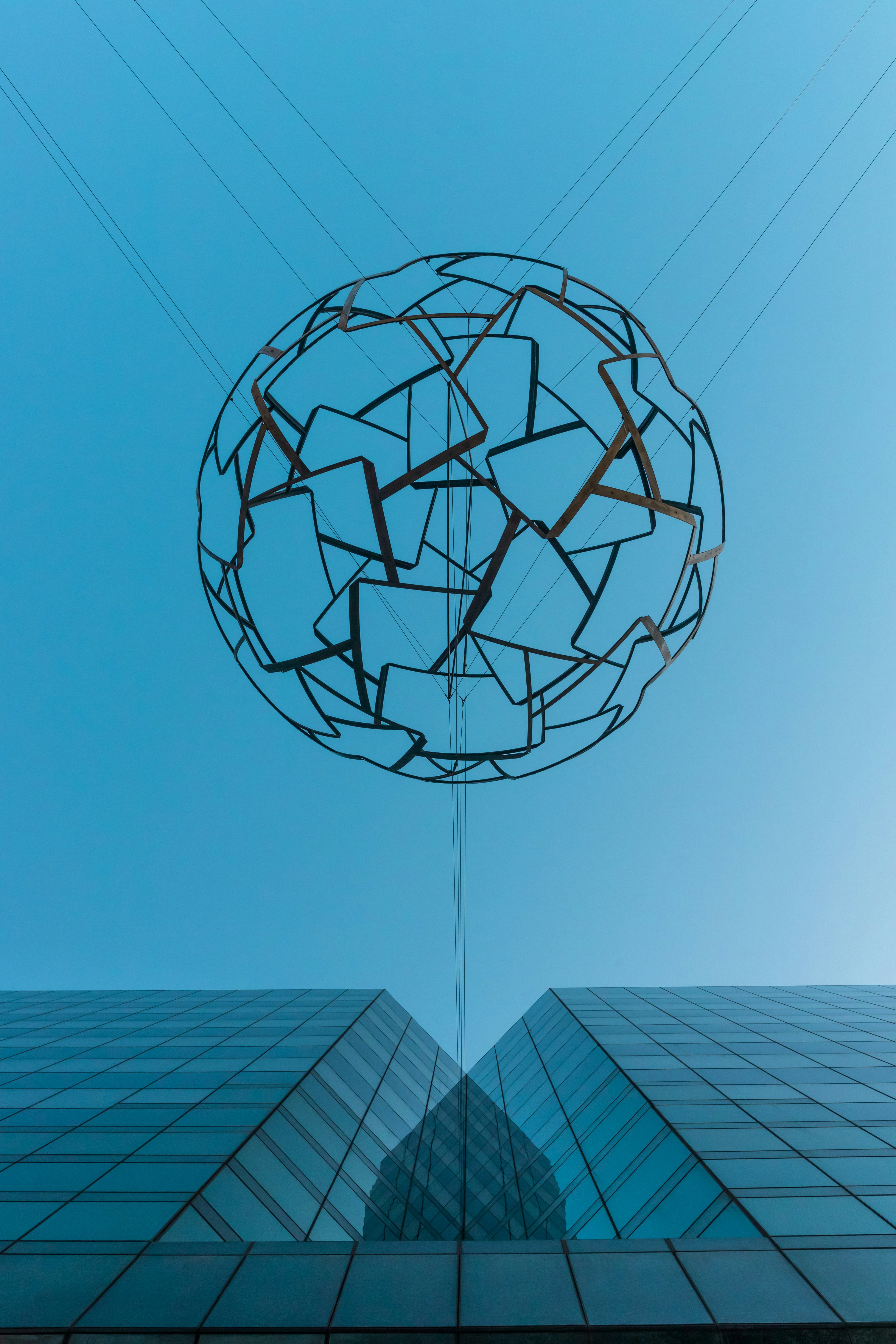 Metal sphere sculpture hanging between two modern glass buildings.