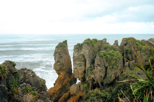 brown rocky mountain beside body of water during daytime in Pancake Rocks New Zealand