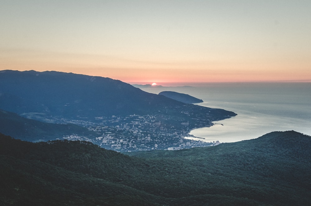 aerial view of green mountains and body of water during sunset