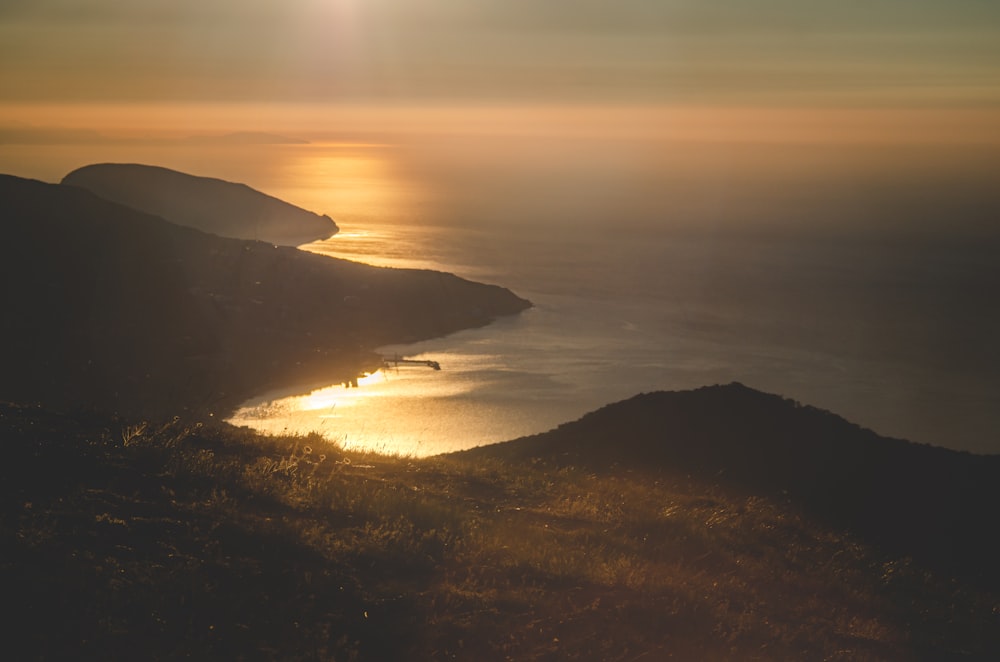 silhouette of mountain near body of water during sunset