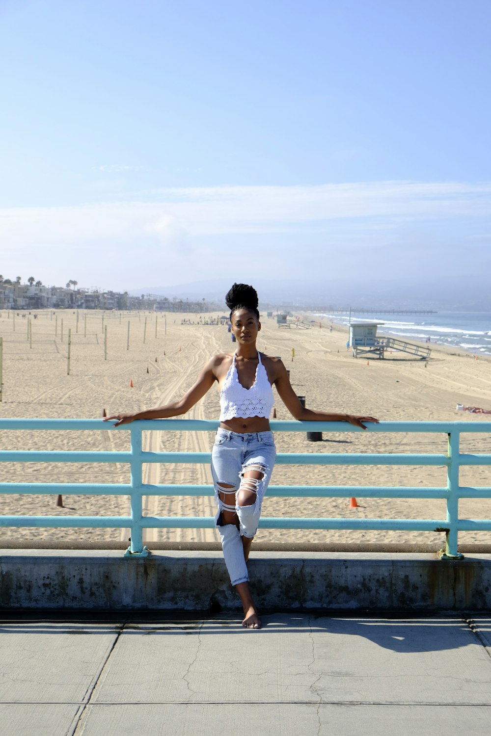 woman in white tank top and blue denim shorts sitting on blue wooden fence during daytime