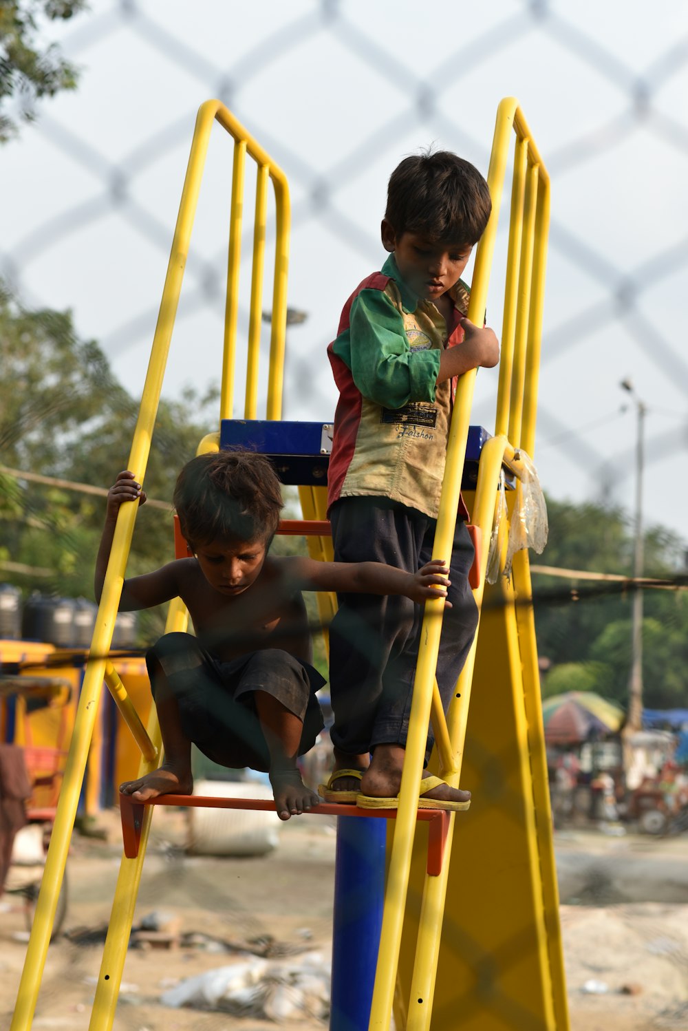 boy in green and black jacket sitting on yellow metal ladder during daytime