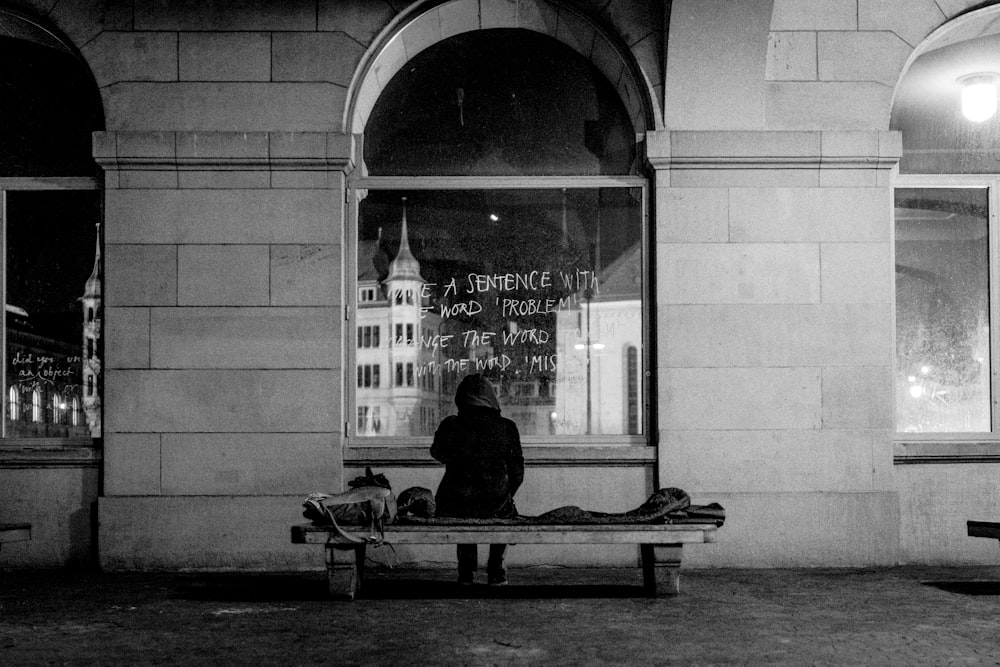 Mann sitzt auf Bank vor Glasscheibe