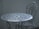 An intricately designed white metal table with a matching chair, set against a plain, muted background. The furniture features floral patterns and detailed craftsmanship, adding a vintage or classic aesthetic.