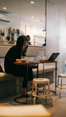 A stylish lifestyle shot of a young creative working on a laptop in a sunlit café with minimalist decor.