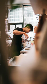 Barista pouring specialty coffee into a fine white cup with soft natural light.