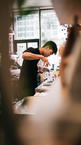 A welcoming barista gently pouring freshly brewed coffee into a ceramic cup, with soft Madini-Hijazi decor in the background.