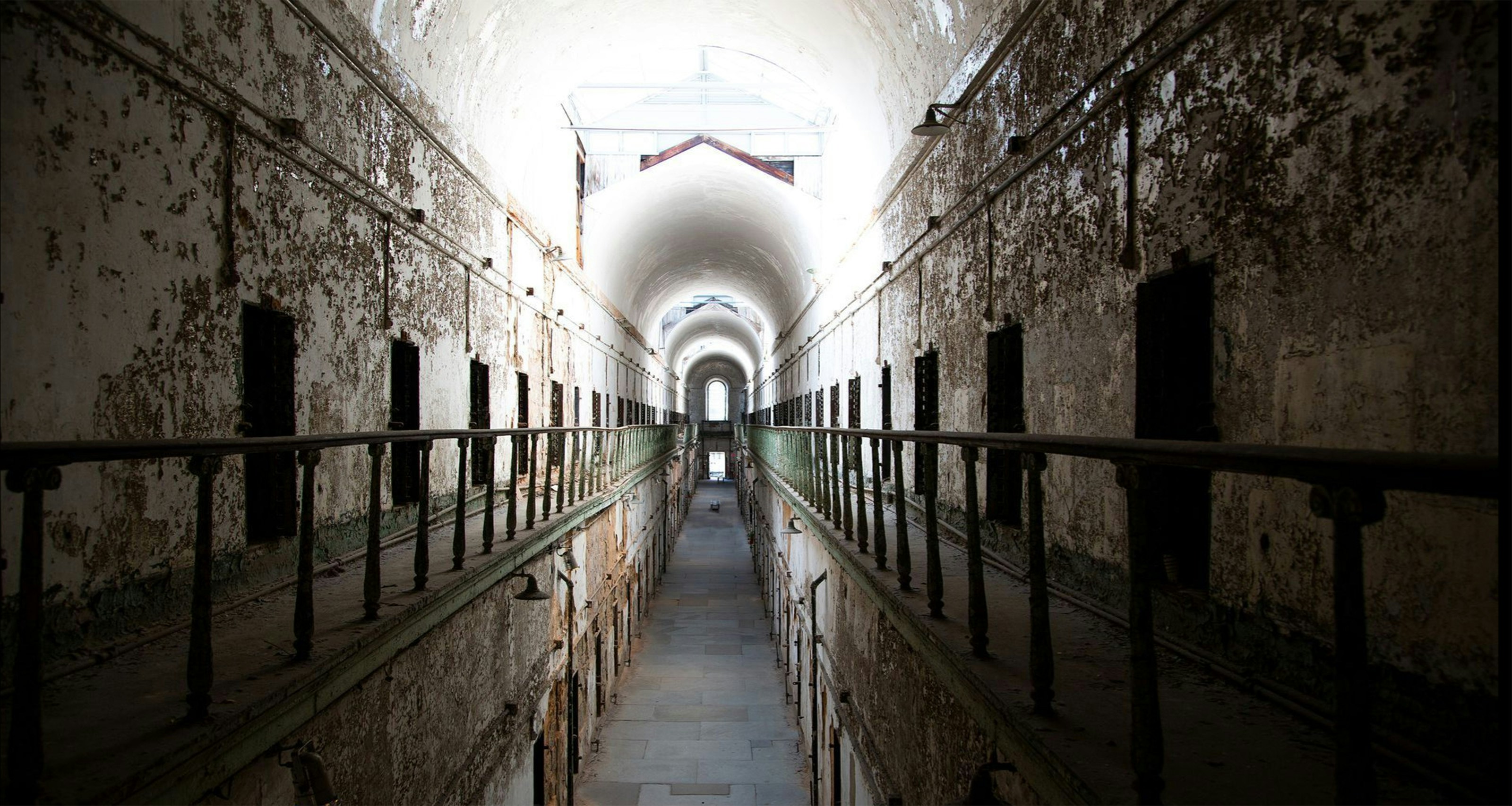 Crumbling cellblock corridor inside Eastern State Penitentiary with peeling paint and haunting light