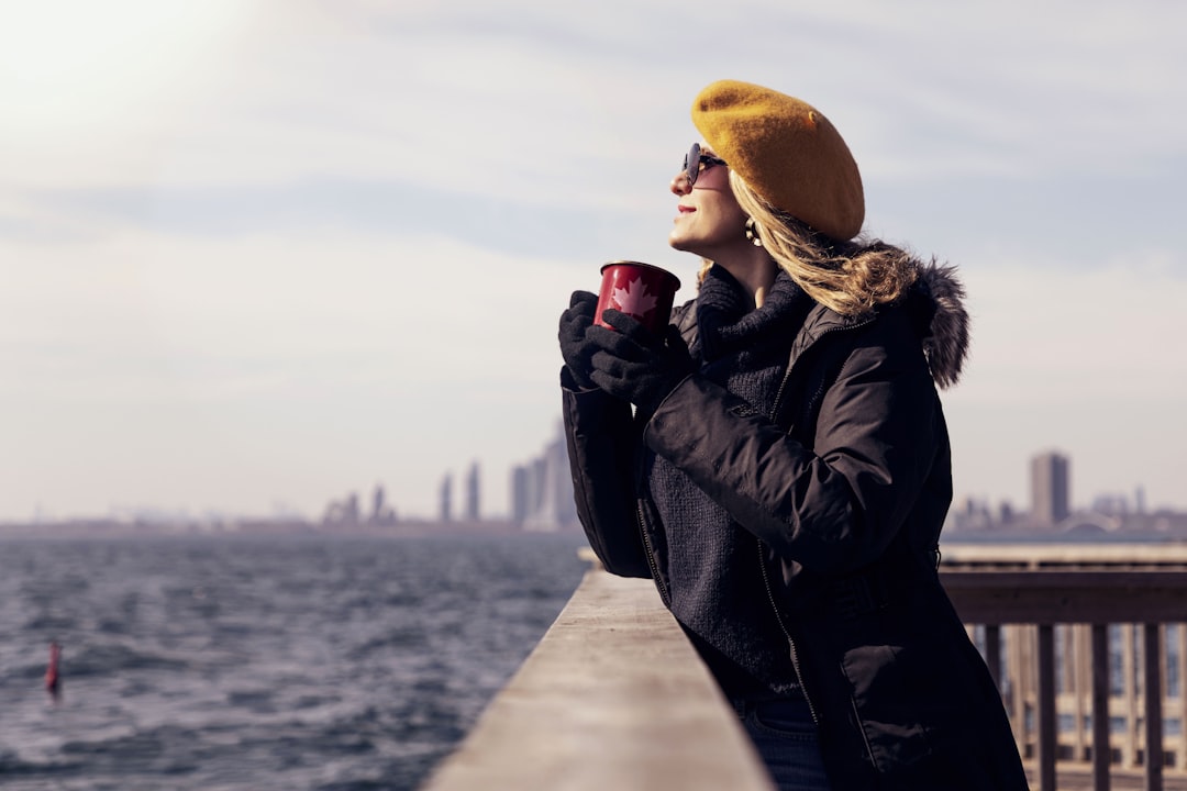 woman in black leather jacket and brown knit cap holding red ceramic mug