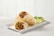 Two burritos filled with ingredients like ground meat, black beans, corn, diced peppers, and cheese are placed on a white rectangular plate. Lime wedges and cilantro garnish the display. The background is a light wooden texture.