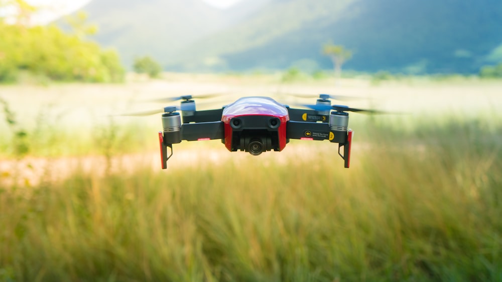 blue and black drone flying over green grass field during daytime