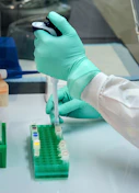 Scientist pipetting liquid samples into vials during laboratory testing.