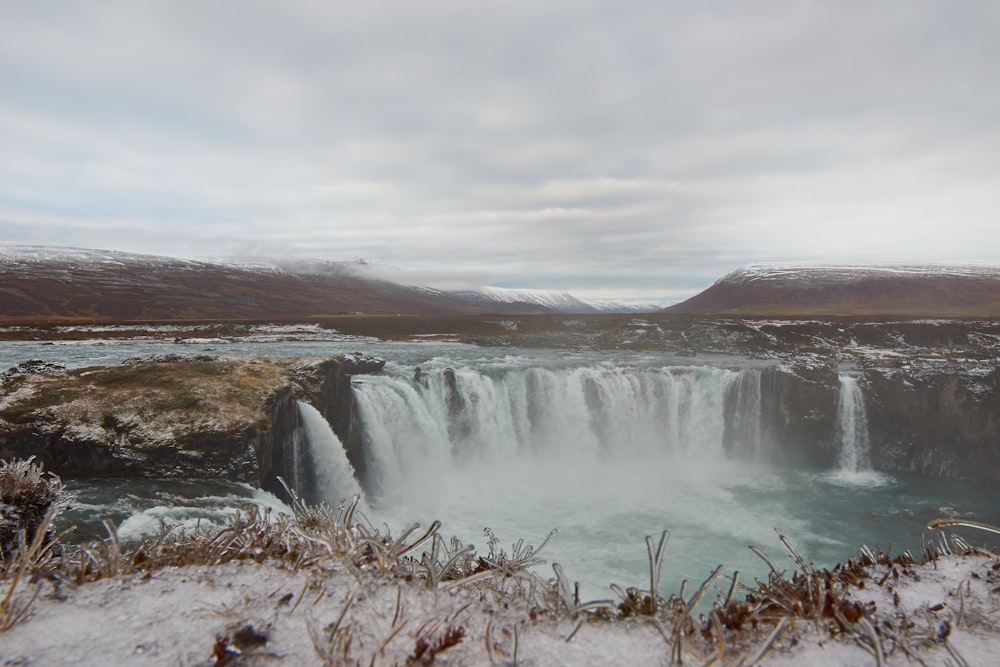 waterfalls near brown mountain under white sky during daytime