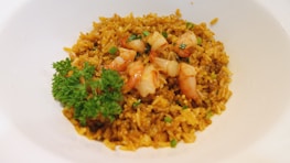 A plate of golden-brown fried rice garnished with pieces of shrimp and fresh green parsley in the center. The rice is evenly cooked, with visible green onions enhancing the presentation.