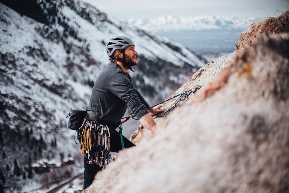 homem na jaqueta preta escalando a montanha durante o dia