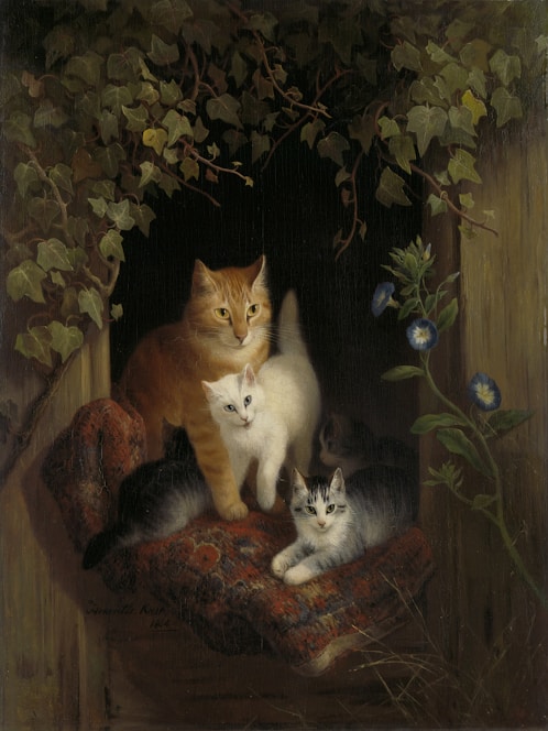 A family of cats, including one adult and three kittens, rests on a patterned red cushion in a wooden enclosure. The setting is adorned with lush green ivy and a few blue flowers, creating a serene and cozy environment.
