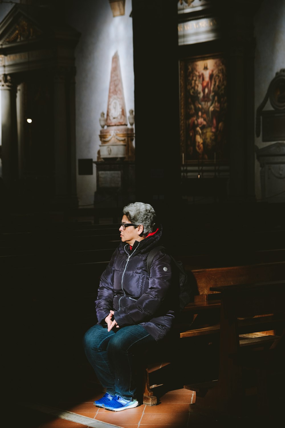 man in black leather jacket and blue denim jeans sitting on brown wooden bench